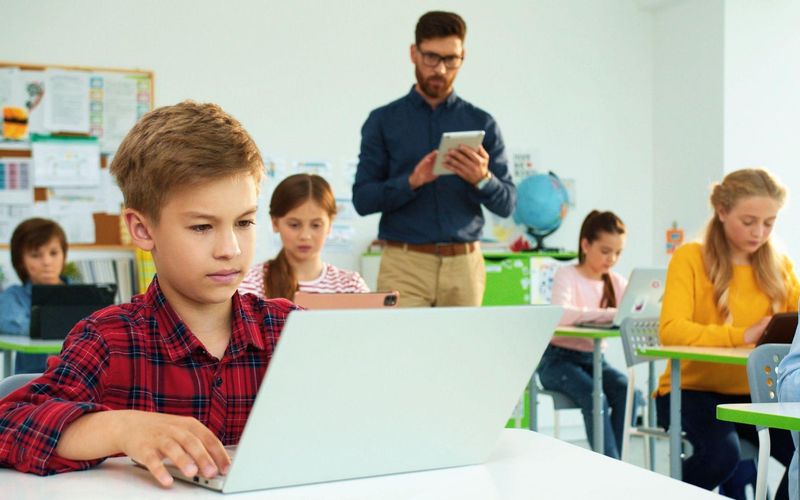 children in classroom behind laptops